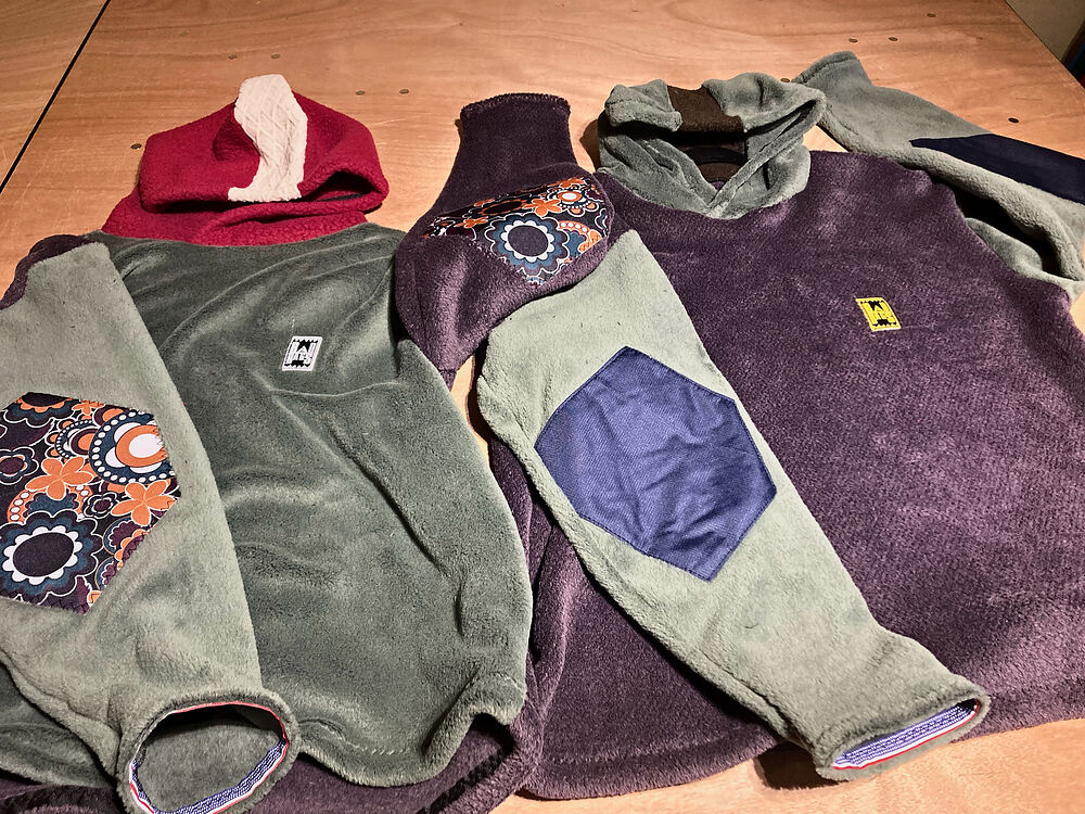 Three fleece hoodies laid out on a plywood table, one with a floral elbow patch