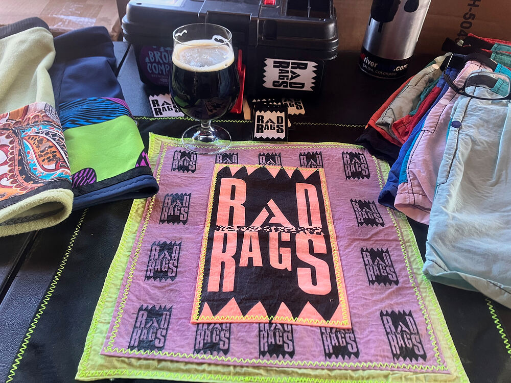 The pink Rad Rags banner on a pop-up table with a glass of beer and folded fleece
