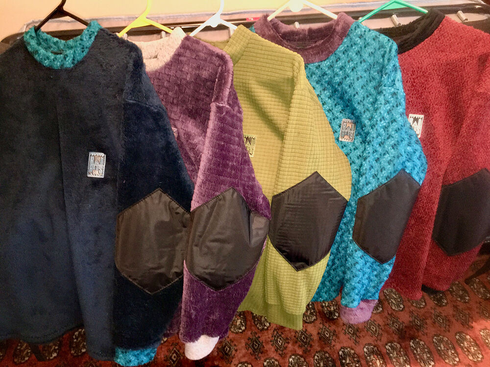 Five fleece crewnecks with black elbow patches hanging in a row