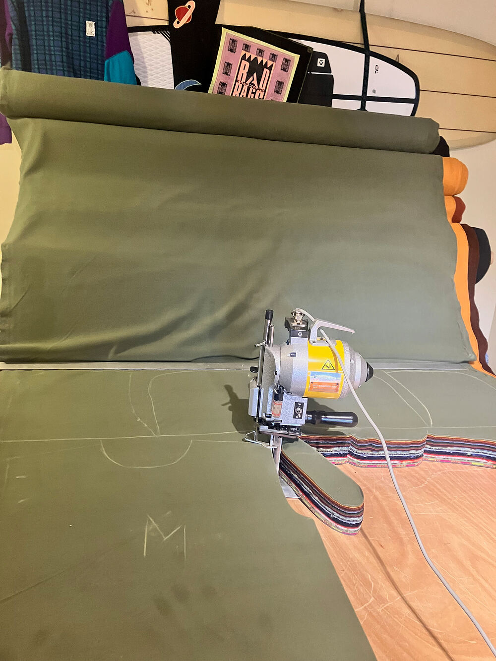 An electric cutter on a long sheet of olive fleece, with a Rad Rags banner behind