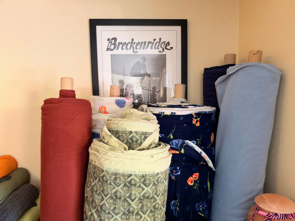 Bolts of fleece standing in front of a framed vintage Breckenridge ski poster