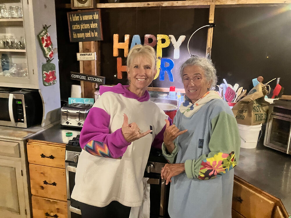 Two women in Rad Rags hoodies throwing shakas in a kitchen