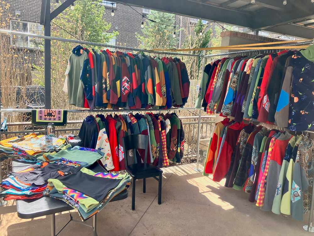 Rad Rags pop-up under a patio roof, two racks and a table full of fleece