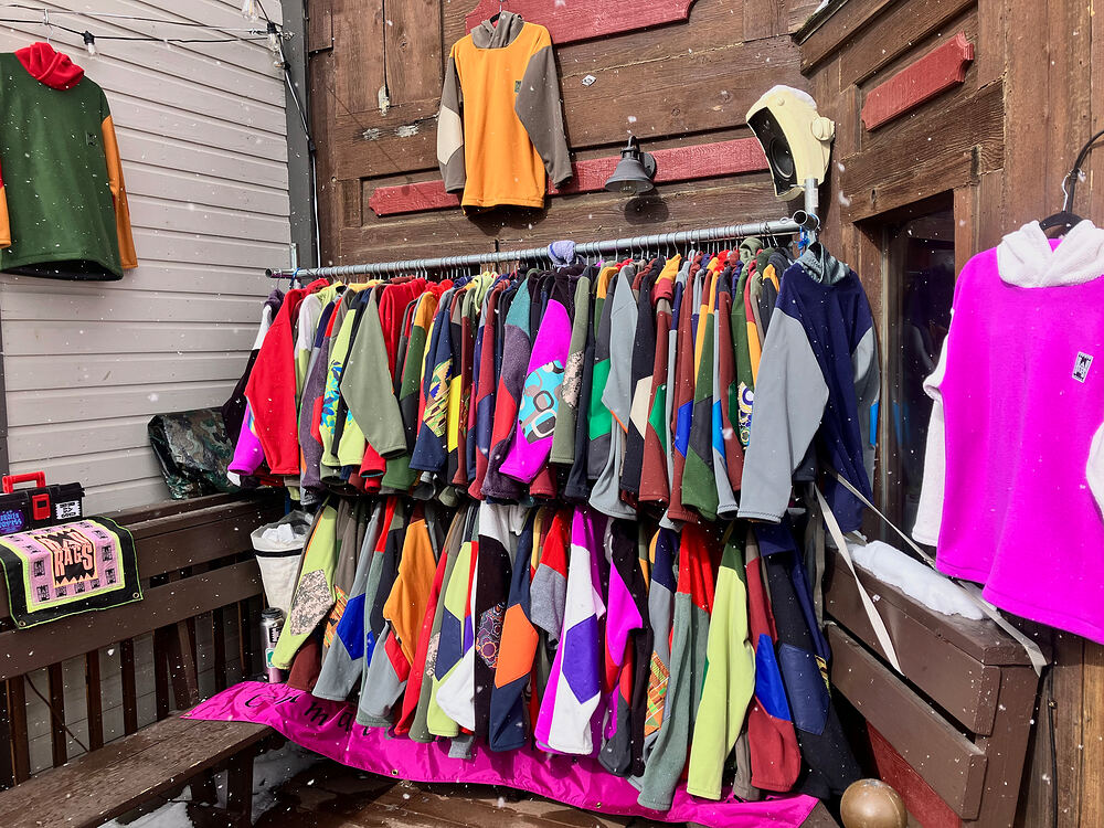 A rack of patchwork fleece outside an old wooden building in the snow