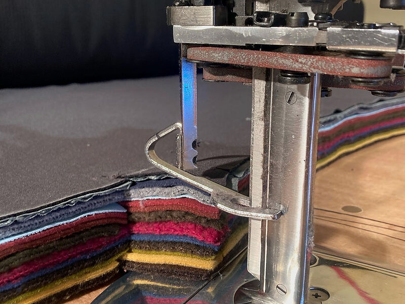 A cutting machine's blade going down through a tall stack of colorful fleece layers