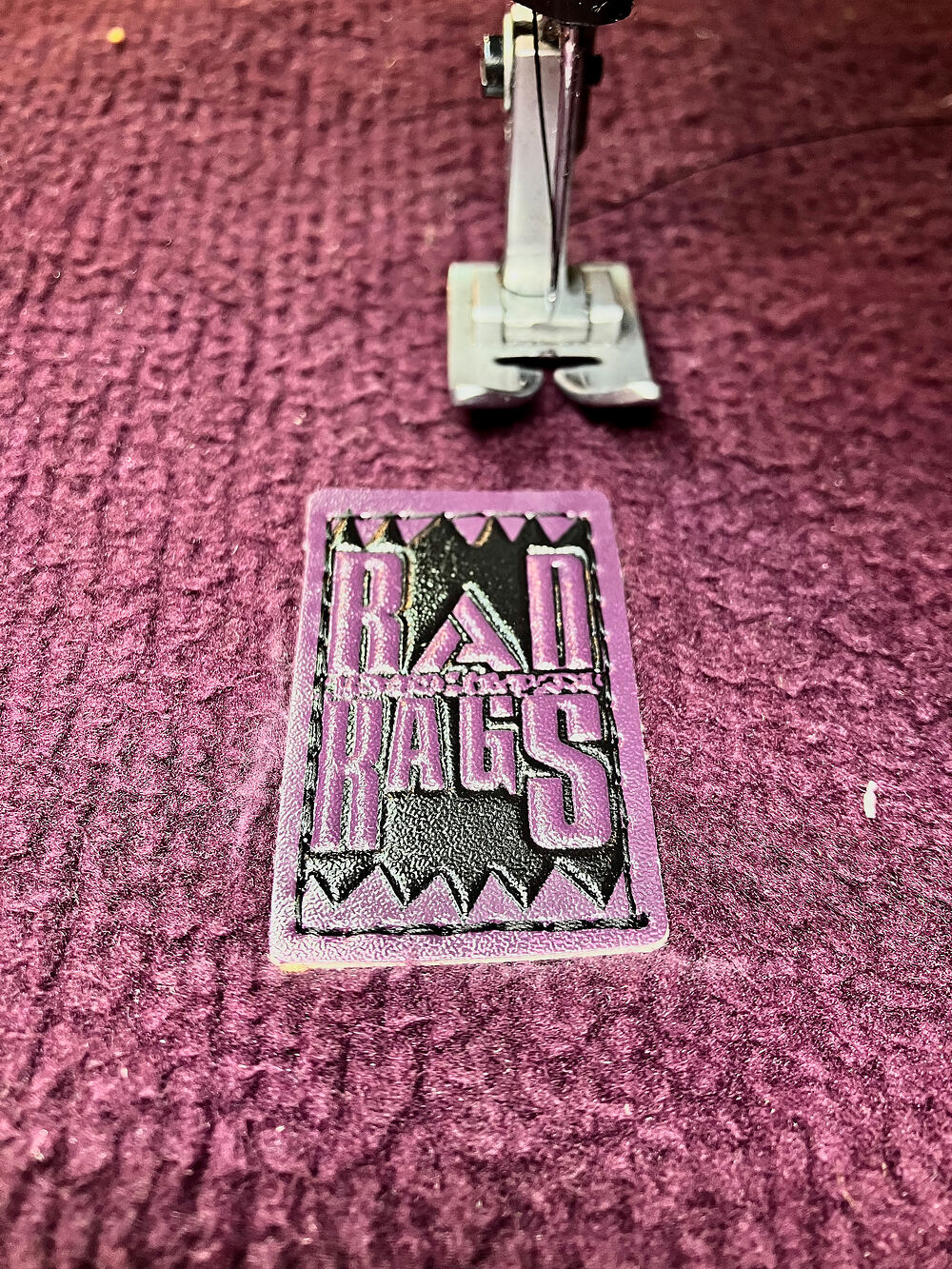 Sewing machine stitching a Rad Rags label onto maroon fleece