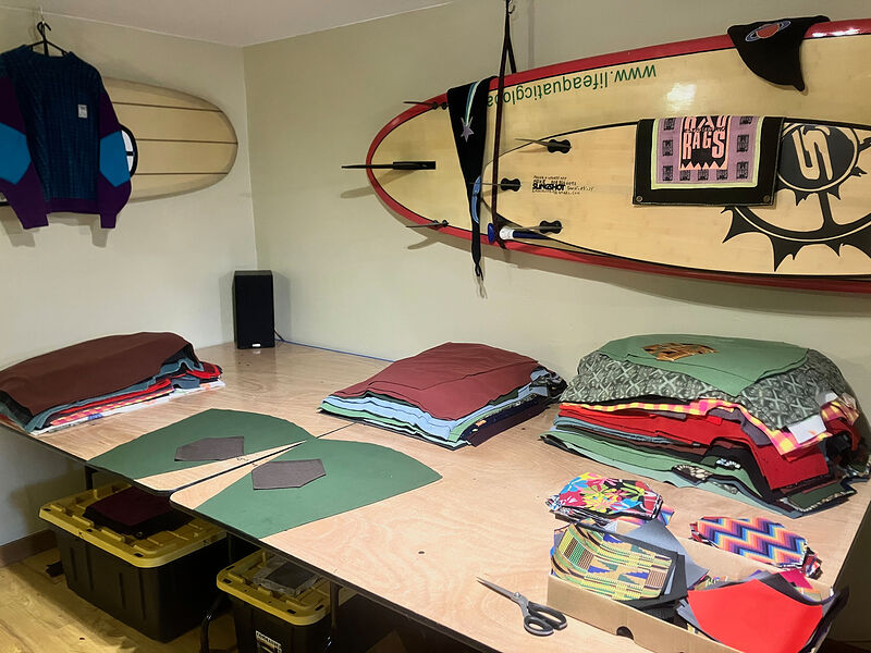 The workshop: a long cutting table with pattern pieces and stacks of fleece, surfboards and a Rad Rags banner on the wall
