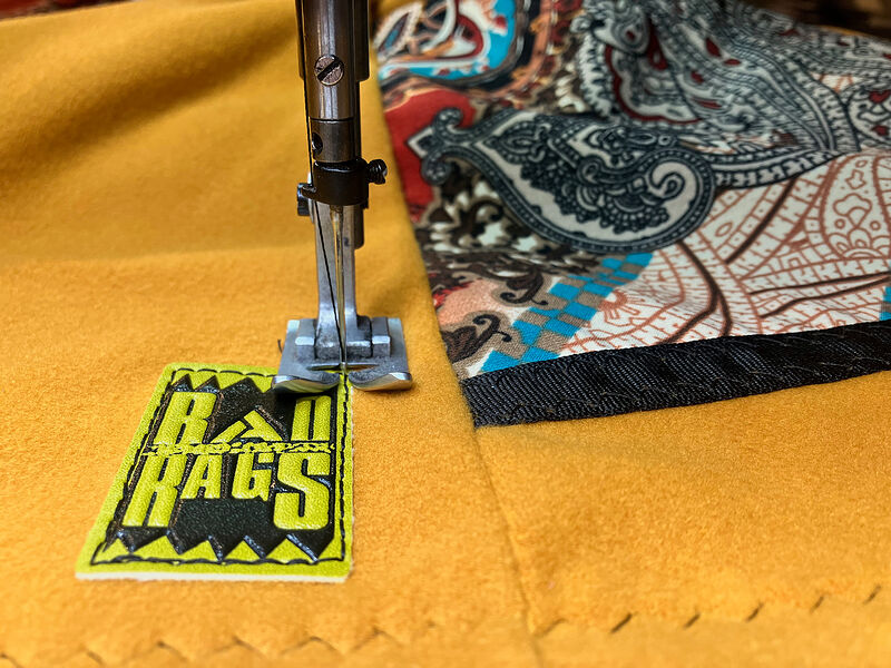 Sewing a yellow Rad Rags label onto mustard fleece next to a paisley panel