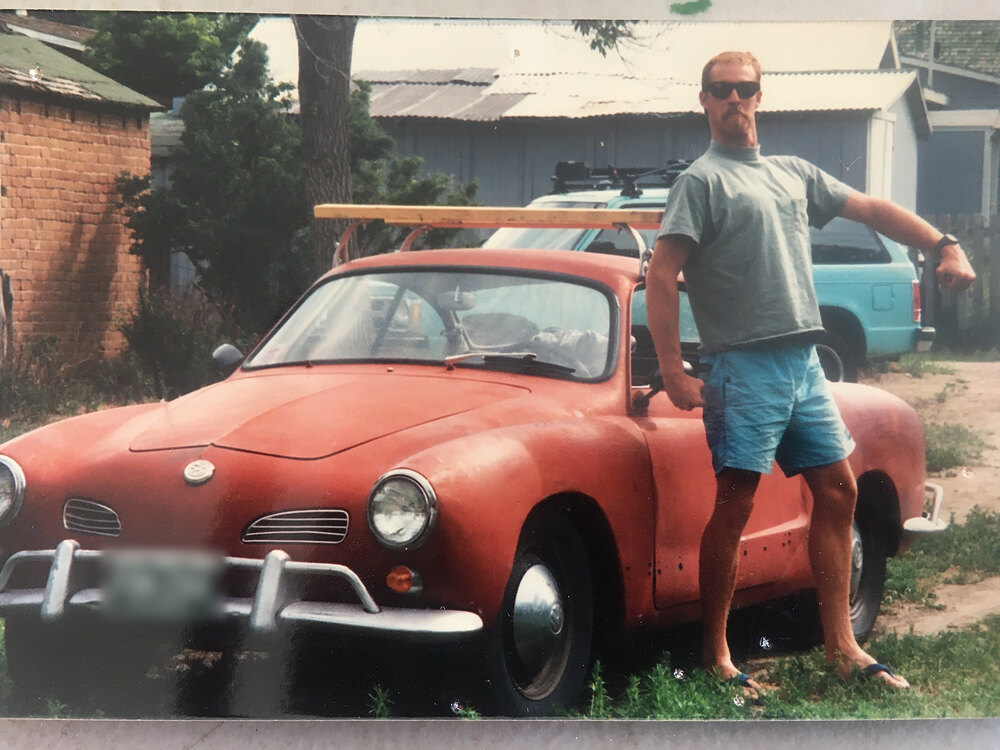 Old photo of a man in sunglasses and shorts beside a red Volkswagen Karmann Ghia