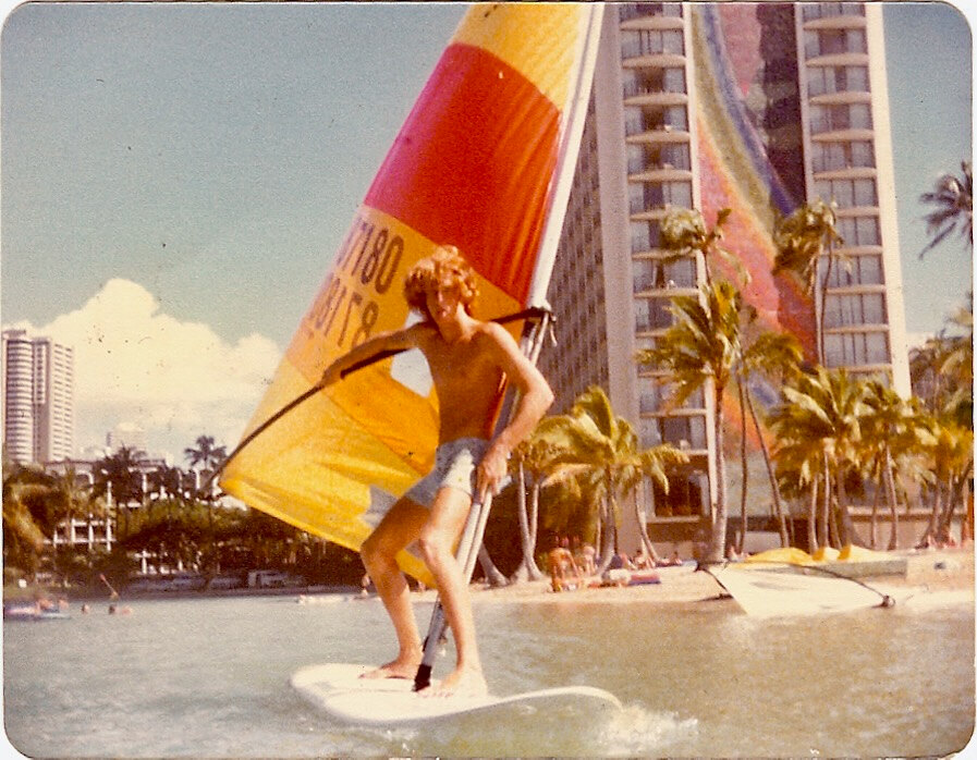 Vintage photo of a young windsurfer on the water at Waikiki, in front of palm trees and beachfront hotels