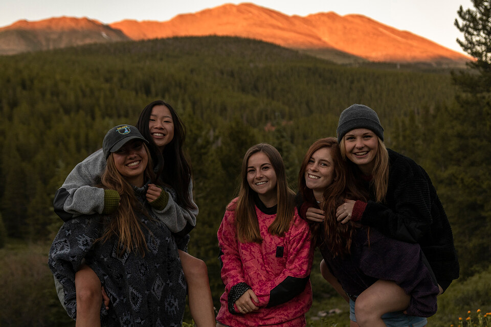 Six friends in fleece laughing together as alpenglow lights the peaks