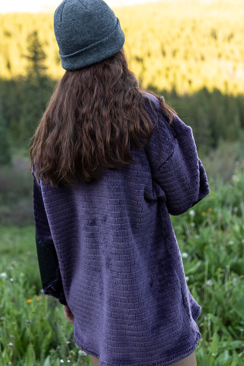 Model in a lavender fleece and gray beanie looking out at the mountains