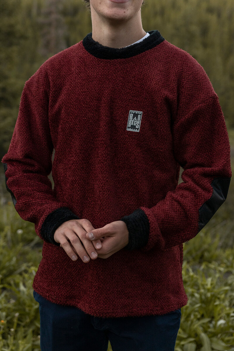 Model in a maroon fleece crewneck with black cuffs in a mountain meadow
