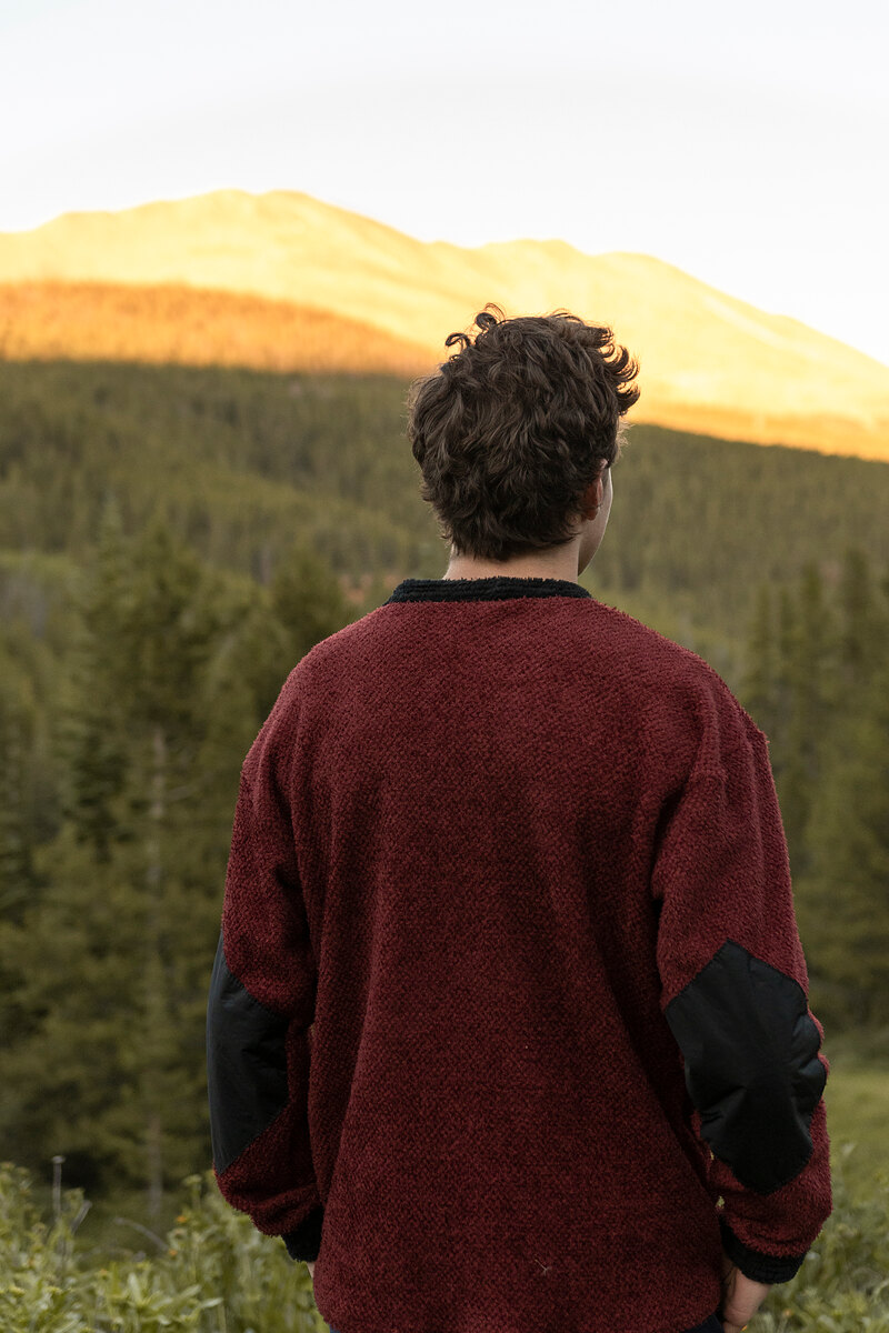 Back of a maroon crewneck with black elbow patches facing a sunlit ridge