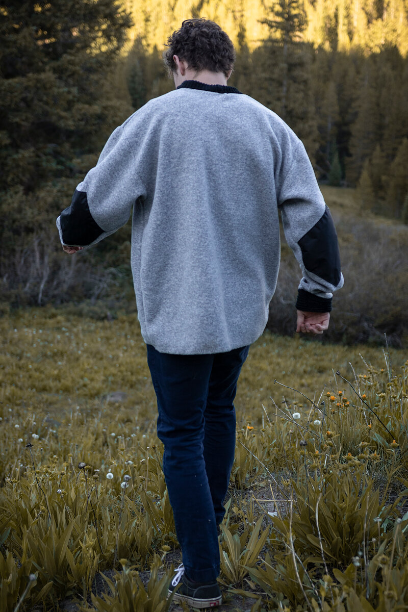 Model walking away through the meadow in a gray crewneck