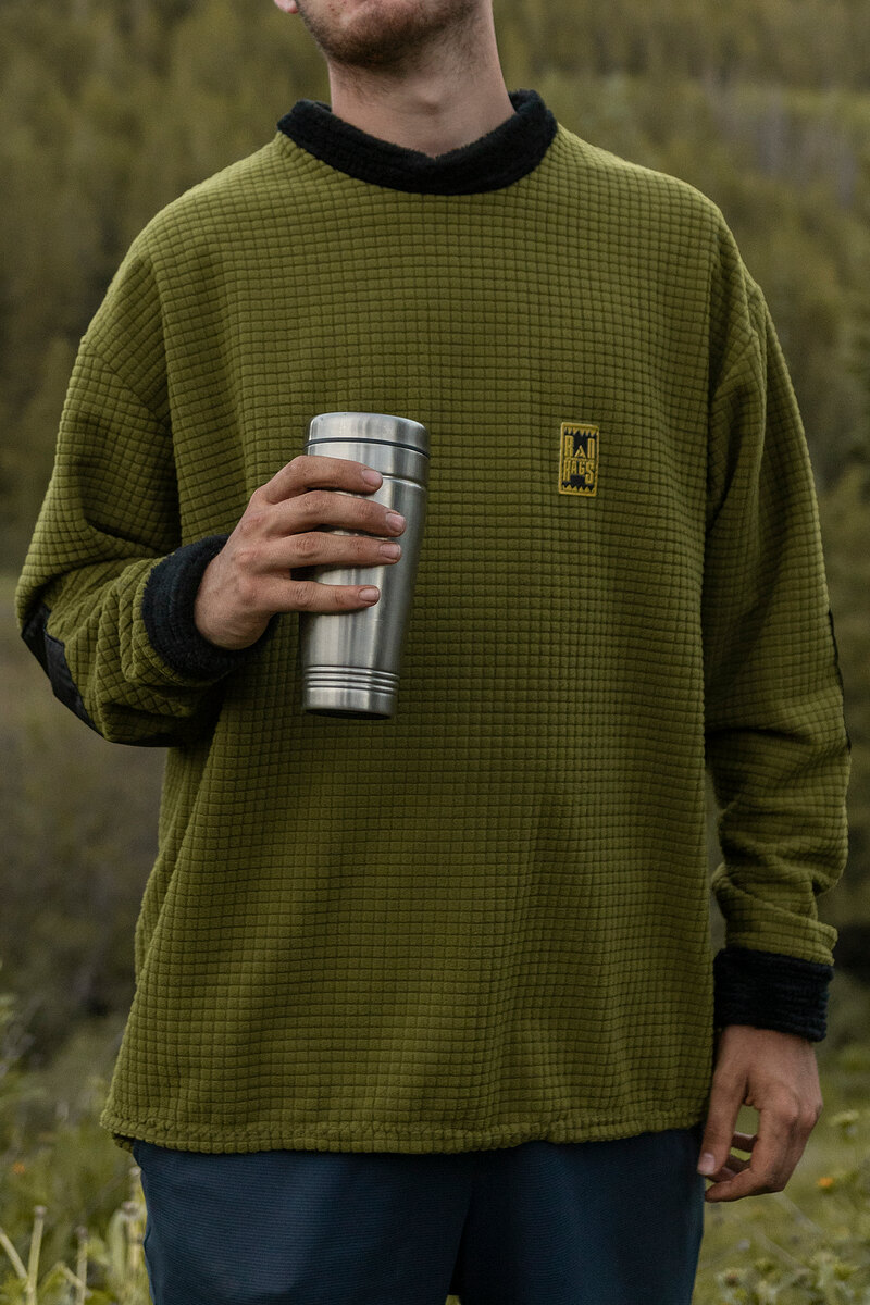 Model in an olive grid fleece holding a steel tumbler