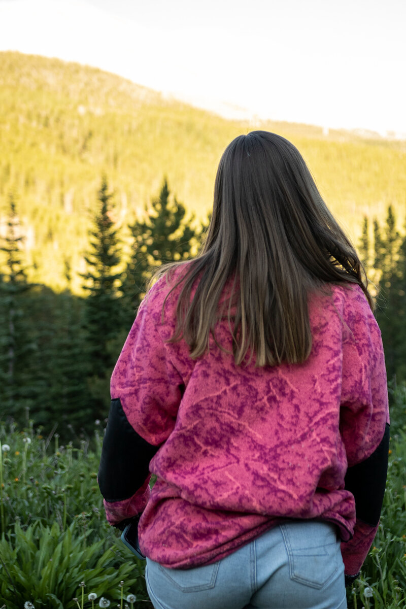 Back of a pink print fleece with black sleeves, pine forest behind