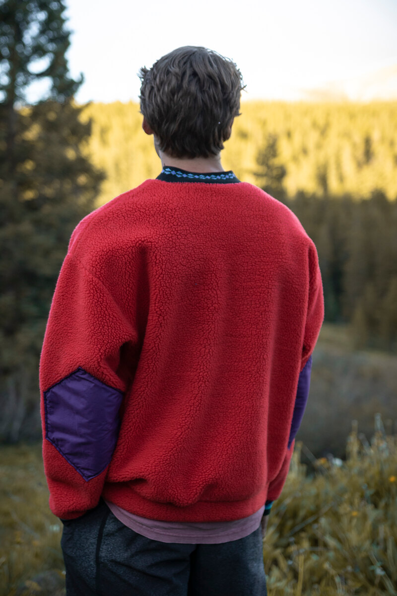 Back of a red crewneck with purple elbow patches in a mountain valley
