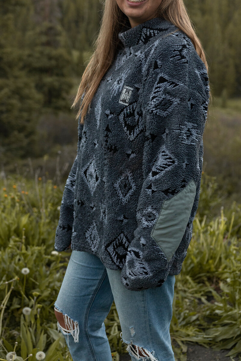 Model in a gray southwest-pattern fleece and ripped jeans in a meadow