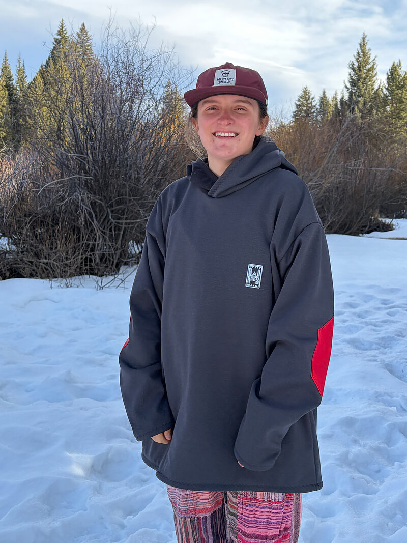 Smiling person in a charcoal Rad Rags hoodie and a cap, standing in the snow
