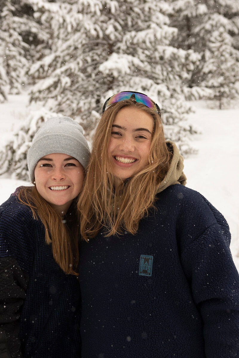 Two friends in navy fleece smiling cheek to cheek in the snow