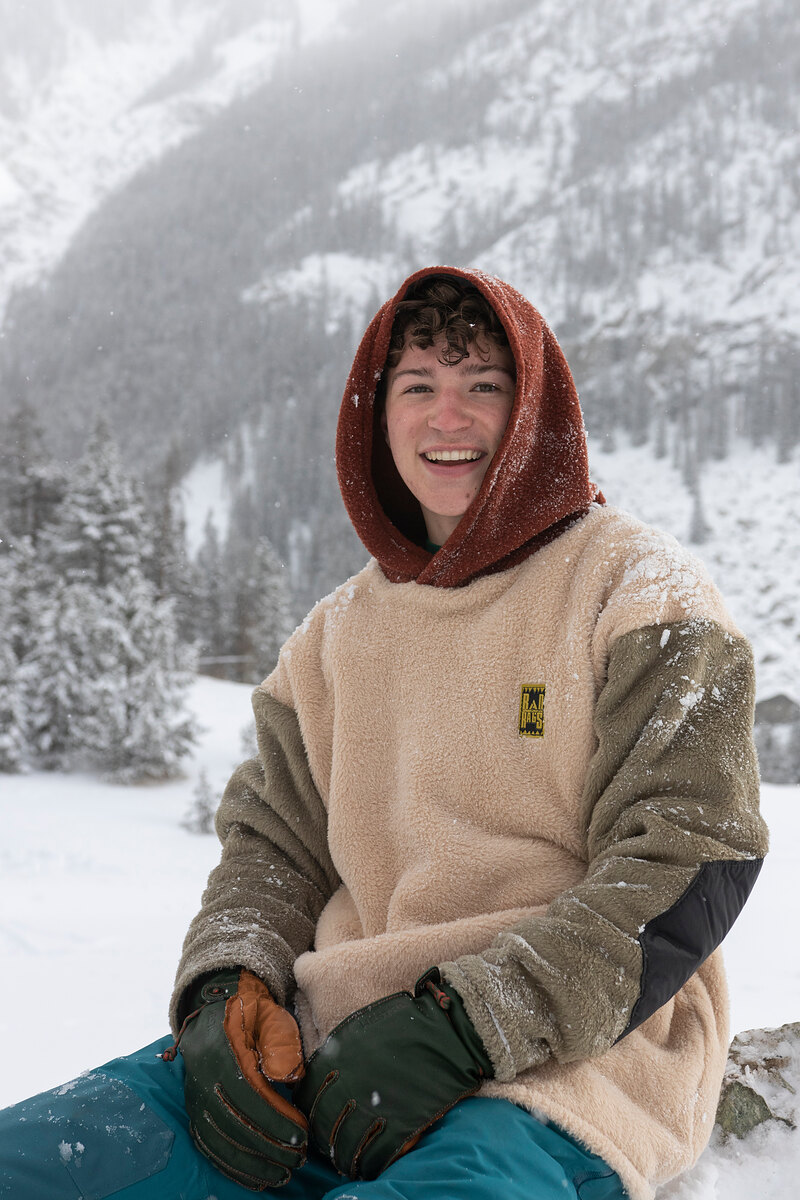 Smiling model in a cream and olive sherpa hoodie sitting in the snow