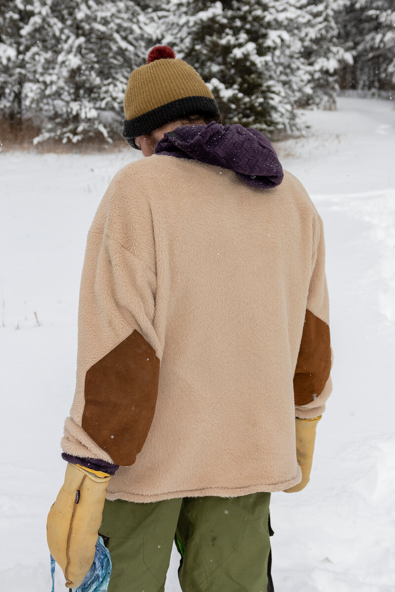 Back of a cream fleece with brown elbow patches and a pom beanie