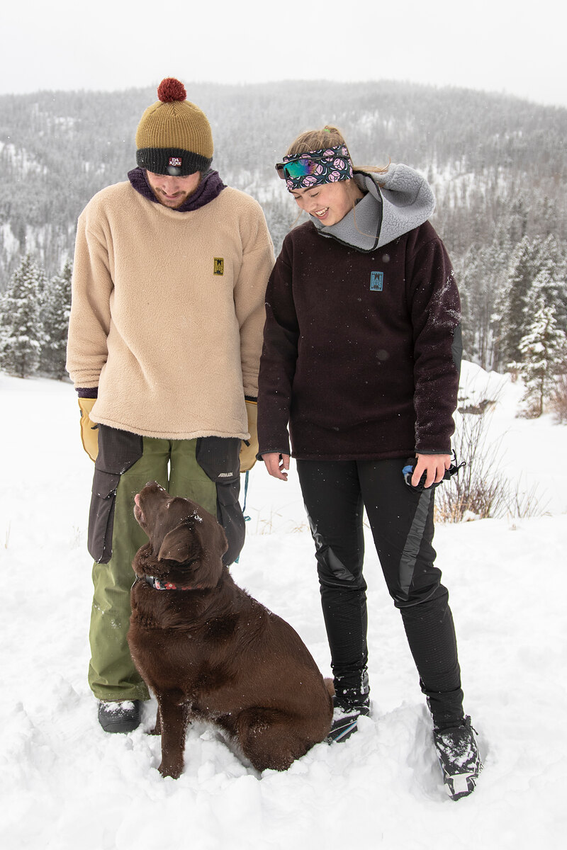 Two friends in cream and black fleece with a chocolate lab in the snow