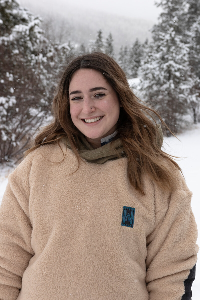 Smiling model in an oatmeal sherpa pullover in a snowy forest