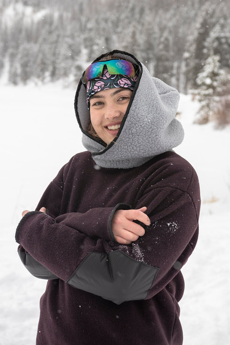 Smiling model in a plum fleece with a gray hood, arms crossed