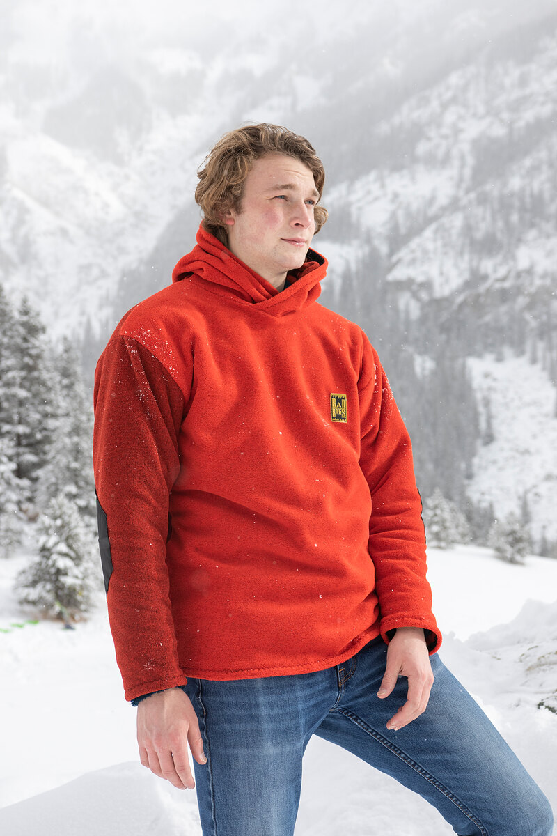 Model in a red-orange fleece hoodie with snowy mountains behind