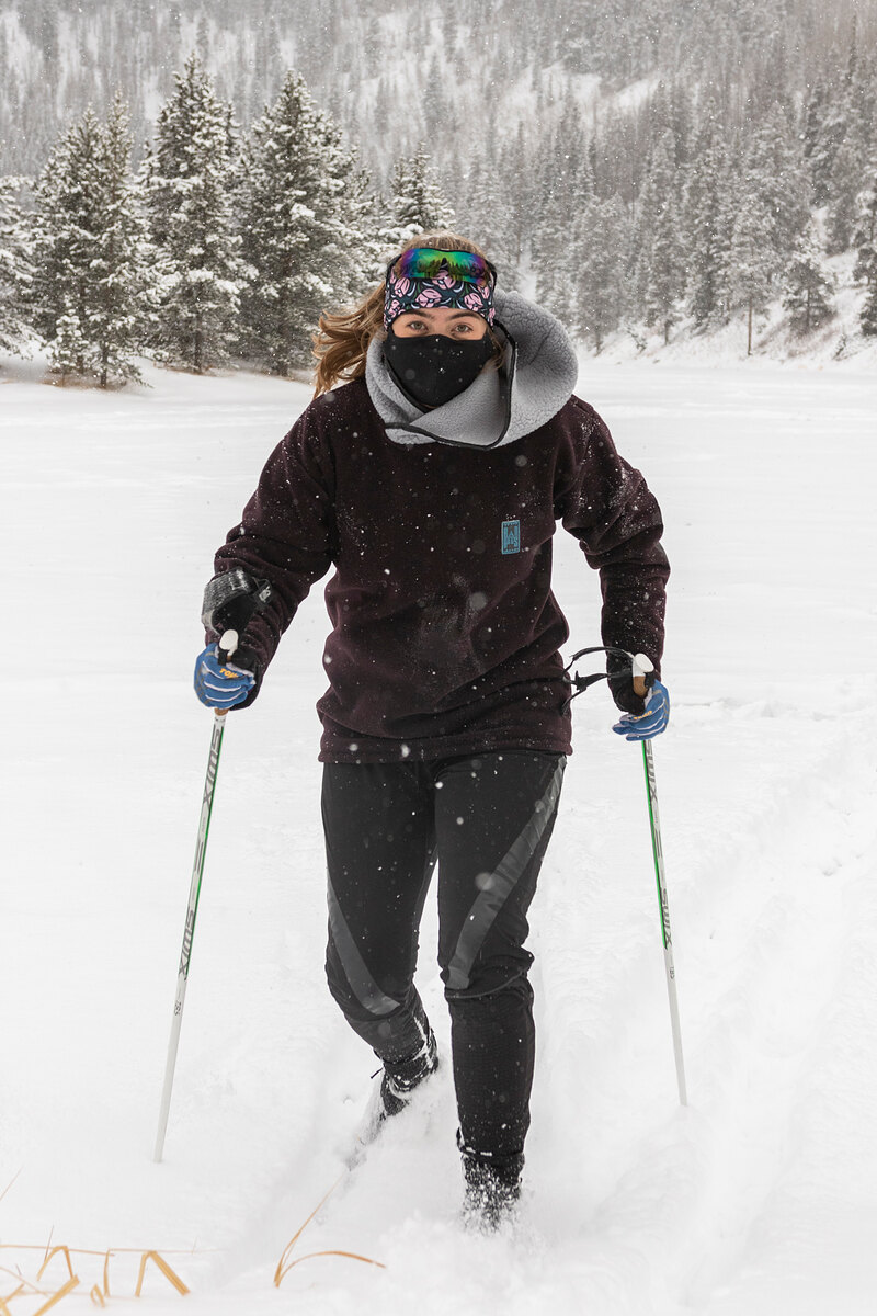 Skier with poles in a dark fleece and goggles in falling snow