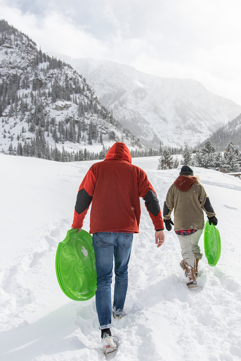 Two friends carrying green sleds up a snowy valley