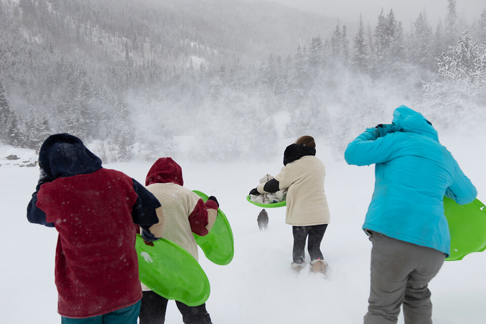 Friends running with green sleds through blowing snow