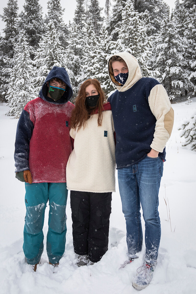 Three friends in fleece hoodies standing in fresh snow under pine trees